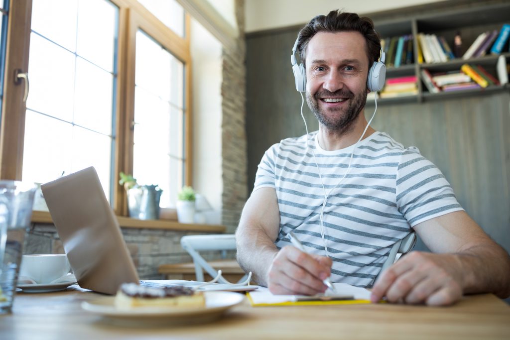 Portrait of smiling man with headphones writing in his diary at coffee shop