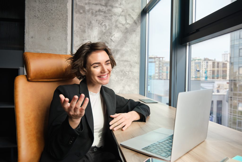 Portrait of corporate woman in office, working, giving presentation, chatting with clients or coworkers on laptop, having online meeting, wearing business suit.